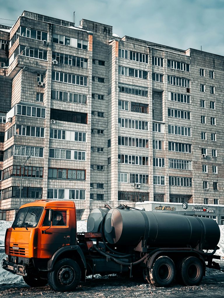 pexels-photo-23228374-23228374 Orange industrial truck parked in front of a high-rise concrete building on a cold day.