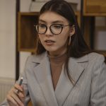 A focused young woman with eyeglasses working in an indoor office setting.