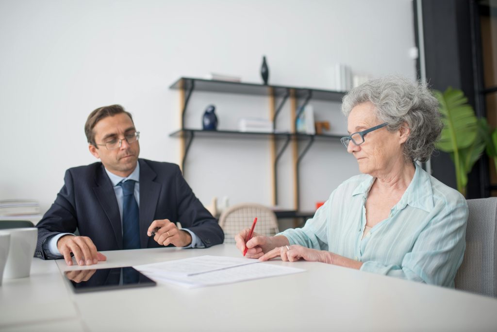 pexels-photo-8441792-8441792 Elderly woman signing paperwork in modern office with consultant.