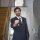 Smiling realtor in a black suit handing keys through an open door inside a modern house.